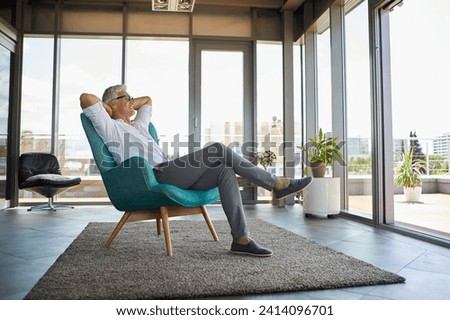 Smiling mature man relaxing in armchair at the window at home Royalty-Free Stock Photo #2414096701