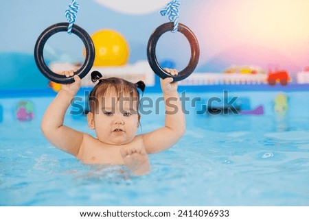 Happy little baby girl swims in pool with trainer, concept development of muscles body and health care of kid.