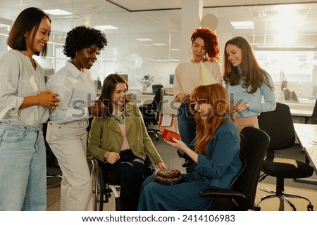 Happy ginger business woman opening a gift while celebrating birthday with multiracial coworkers in the office. Diverse business people making a surprise party for their coworker. Copy space.