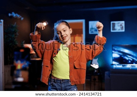 Entertaining kid in dimly lit personal studio joins viral dance craze, recording family friendly video for children audience. Small girl in her apartment does latest internet dancing challenge Royalty-Free Stock Photo #2414134721