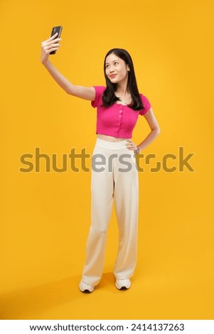 Full body photo of excited young asian woman hold telephone make selfie have good mood isolated on yellow color background