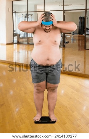 Picture of young fat man checking his weight while standing on the scale in a gym