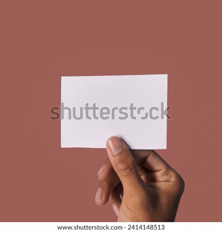 Hand holding up a piece of small white card. isolated on brown background 
