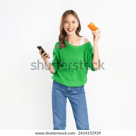 Cheerful young asian woman in green shirt with holding credit card and using smartphone on isolated white background.