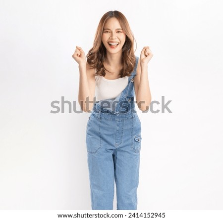 Cheerful beautiful Asian woman wearing jeans overalls with excited doing winner gesture with arms raised isolated on white background. Royalty-Free Stock Photo #2414152945