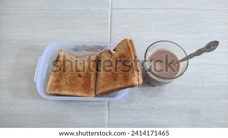 Two toasted bread slices in a lunchbox beside a glass of chocolate milk.