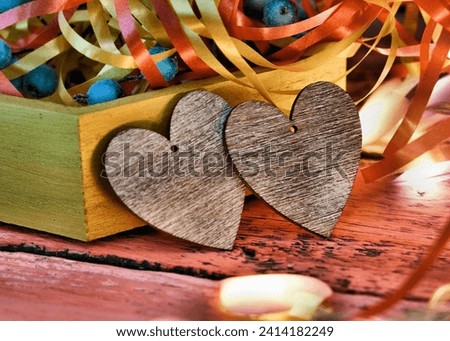 Two wooden hearts on wooden background with blurred lights and box with holiday decorations. Happy Valentines day  