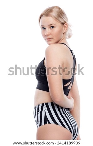 Teenage girl in a swimsuit. Cute smiling young blonde woman wearing black and white striped panties and a black top. Sports and recreations. Isolated on a white background. Vertical.