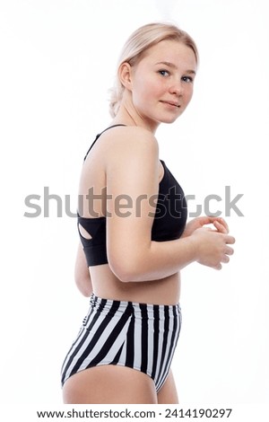 Teenage girl in a swimsuit. Cute smiling young blonde woman wearing black and white panties and a black top. Sports and recreation. Isolated on a white background. Vertical. 