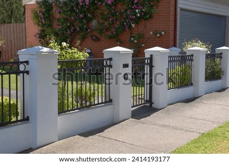 BRICK PILLAR LUXURY FRONT FENCE WITH CIRCULAR WROUGHT IRON FEATURES - Solid cement render columns with peak caps with black metal bar poles with a circle design along the top and front gate Royalty-Free Stock Photo #2414193177