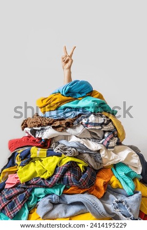Unrecognizable human raises arm reaches out heap of colorful unfolded clothes busy doing wardrobe cleaning isolated over white background. Woman buried under cluttered clothing items. Decluttering Royalty-Free Stock Photo #2414195229