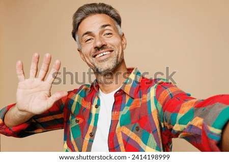 Close up adult man he wear red shirt white t-shirt casual clothes doing selfie shot pov on mobile cell phone waving hand isolated on plain pastel light beige color background studio. Lifestyle concept