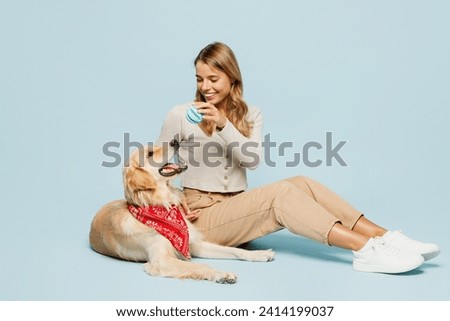Full body happy fun young owner woman wear casual clothes sitting play with her best friend retriever dog in red scarf give ball isolated on plain blue background studio. Take care about pet concept Royalty-Free Stock Photo #2414199037