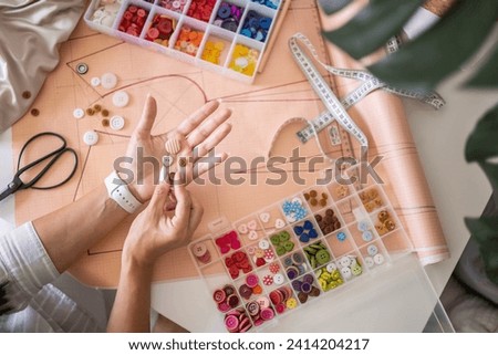Woman tailor choosing sew button round heart shape creating clothes garment at studio top view closeup. Female fashion designer dressmaker trying material for clothing repair enjoy art hobby work Royalty-Free Stock Photo #2414204217