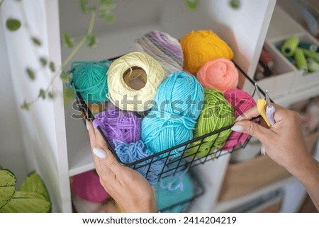 Female hands placing basket with colored ball of yarn for art crochet knitting ribbon cotton wool thread for hobby. Woman tailor sewing materials comfortable storage cupboard arrangement organize Royalty-Free Stock Photo #2414204219