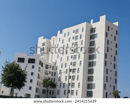 Building with White clouds over blue sky, White color Building view having Ornamental clouds and Blue SKY background, Sky scraper or building with black glass windows, building full view  Royalty-Free Stock Photo #2414215639