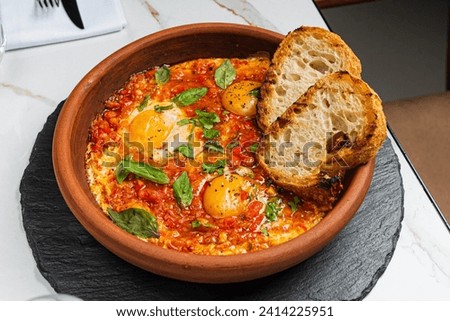 Shakshuka with eggs, tomatoes and bread Royalty-Free Stock Photo #2414225951