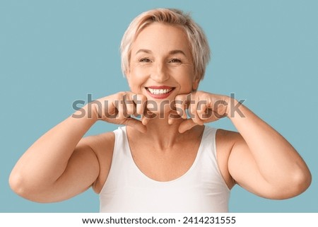 Beautiful mature woman doing face building exercise on blue background, closeup