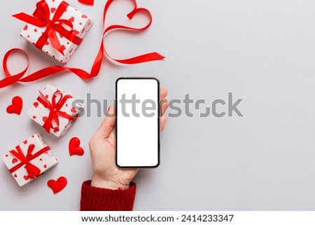 Woman hand holding mobile phone with blank screen on colored background with hearts, valentine day concept top view flat lay.