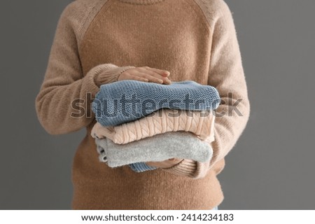 Woman holding stack of different stylish sweaters on grey background