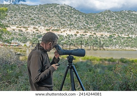 A man birdwatching in a lake with a telescope. Royalty-Free Stock Photo #2414244081