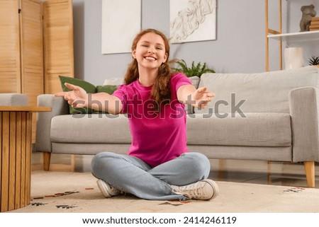 Smiling young redhead woman opening arms for hug at home