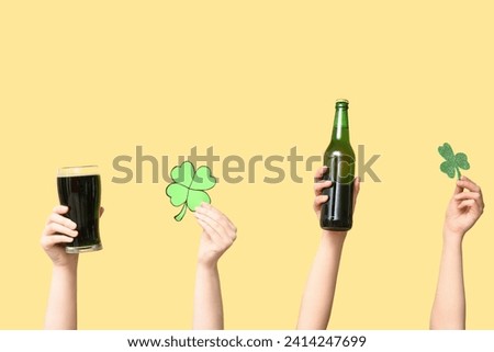 Hands with beer and clover on yellow background. St. Patrick's Day celebration
