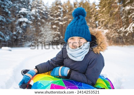 Cute little boy sliding on snow tube in winter forest. Happy childhood