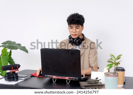Focused Asian graphic designer or editor at work with a laptop, camera, and headphones in a well-organized workspace.