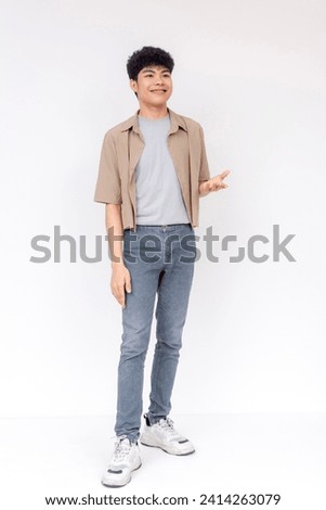 Portrait of a happy young Asian man casually dressed, smiling and gesturing against a white background.