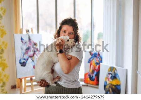 the artist with a white small dog East East Terrier examines her painting
