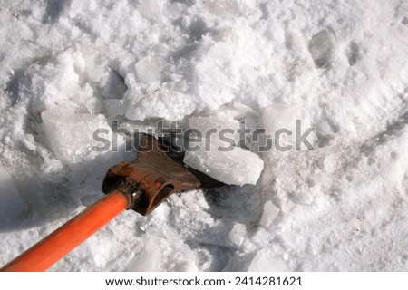 The janitor chops pieces of ice off the ground with a sharp orange iron cleaver. cleans the sidewalk from ice after severe frosts. Cleaning of the territory. Photo from above