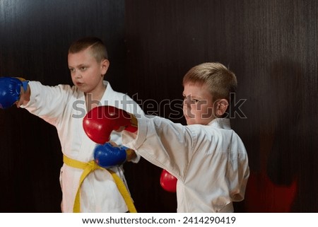 Two athlete boys in karategi with red and blue pads on their hands punch punches Royalty-Free Stock Photo #2414290419