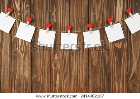 Clothespins with red hearts and empty sheets of paper on string against brown wooden background. Valentines day holiday, romantic concept. Mockup, template, copy space