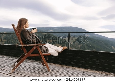 Portrait image of beautiful Caucasian woman holding and drinking hot coffee on balcony, looking at mountains and green nature.