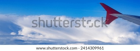 banner part of an airplane wing with a red tip against a background of bright blue sky and snow-white clouds