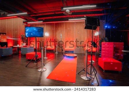 360 spinner photo booth setup in an event space with ambient red lighting, red carpet, lounge furniture, and dynamic blue laser lights.