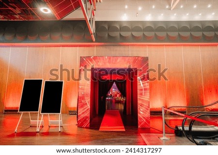 entrance with dynamic red lighting effects leading to an event space, flanked by blank signage boards
