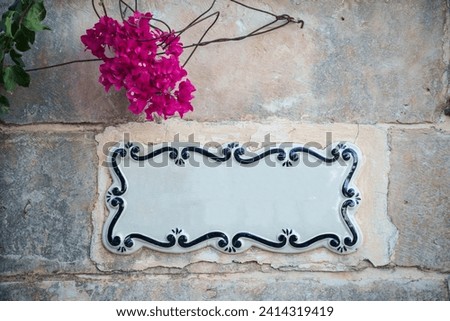 Traditional Maltese home sign board painted on ceramic tile placed on the stone wall without text inside.