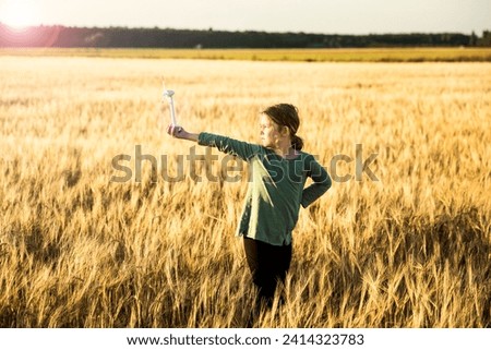 Girl standing in grain field holding miniature wind turbine