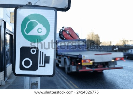 A close up of a Clean Air Zone roadside sign, with an anonymised flatbed lorry passing in the background. Room for copy space in the clear sky