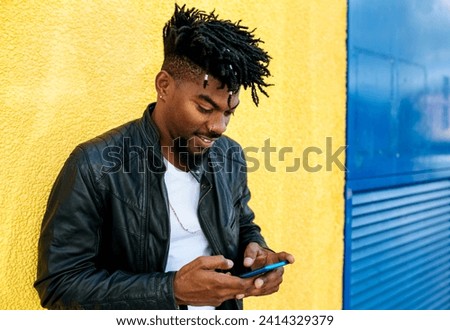 Close-up of mid adult man with locs using mobile phone while standing against wall Royalty-Free Stock Photo #2414329379