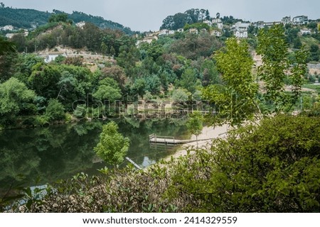 Green leafy bushes framing the Mondego river with wooden bridge in the valley with houses on the hill, Penacova PORTUGAL Royalty-Free Stock Photo #2414329559