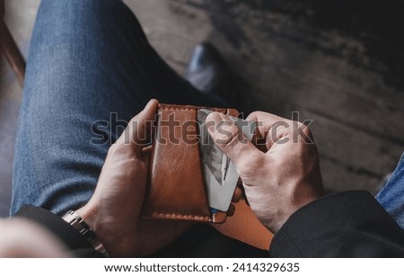 A man takes out credit cards from a brown leather wallet on a dark background, close-up, focus on his hands. The concept of purchasing power and the importance of bank cards in modern life