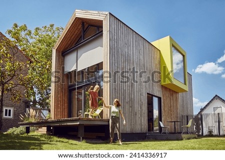 Mother assisting daughter in jumping outside tiny house at yard Royalty-Free Stock Photo #2414336917