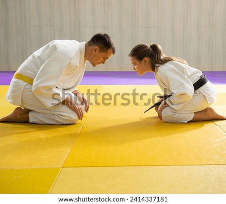 Yellow belt judo man in white judogi and young black belt judo girl in white judogi kneeling  Royalty-Free Stock Photo #2414337181