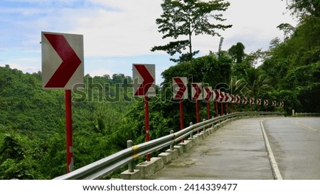 Asphalt road with direction indicators. Signs along the road indicate a right turn. View of a concrete road through the jungle.                               