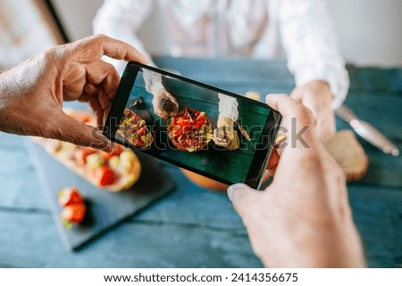 Close-up of man's hands taking a picture with mobile phone eating salad of tomato- pomegranate- papaya and olives- with papaya with fruits on the side and with glass of wine