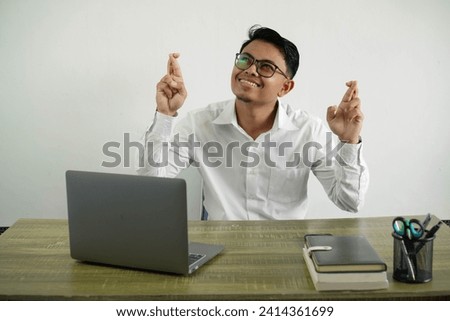 young asian businessman in a workplace with fingers crossing and wishing the best, wear white shirt with glasses isolated