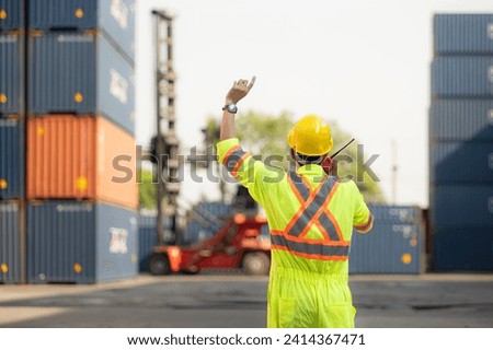 Workers in the import and export industry use walkie talkies to communicate with drivers of reach stacker containers in an empty container warehouse. Royalty-Free Stock Photo #2414367471